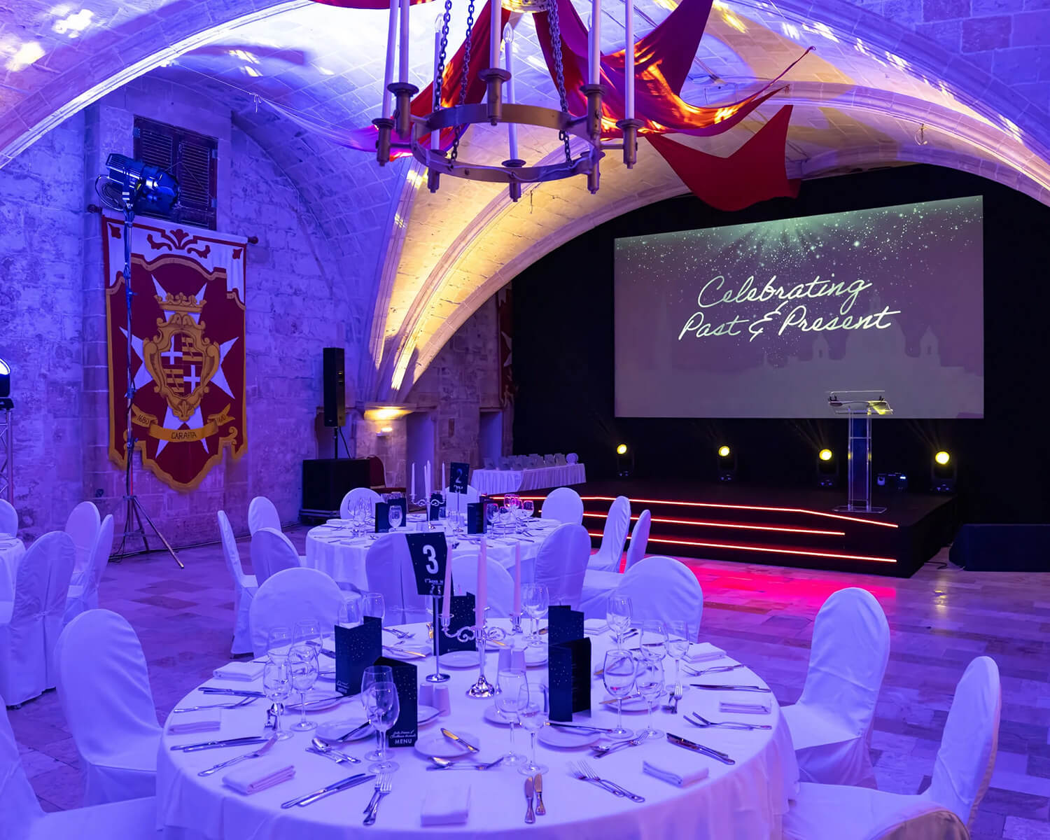 Evening Gala dinner setup with round tables facing the stage displaying 'Celebrating Past & Present'