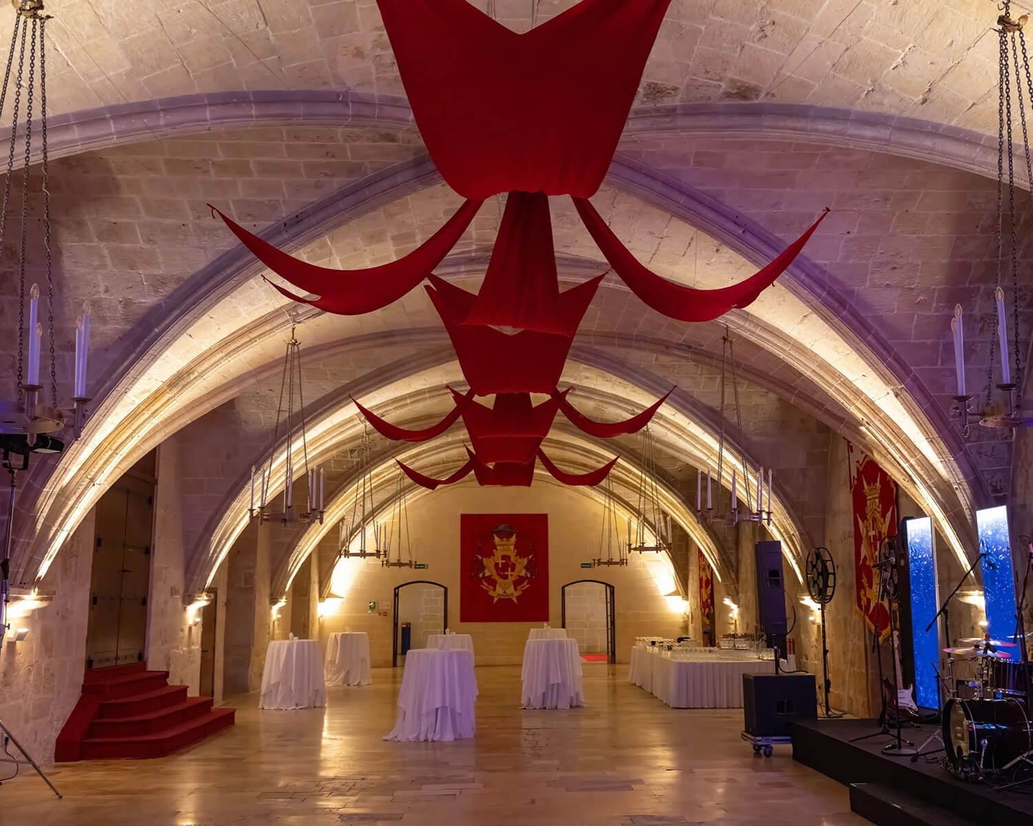Gala dinner setup in historic vaulted hall with red ceiling drapes and cocktail tables