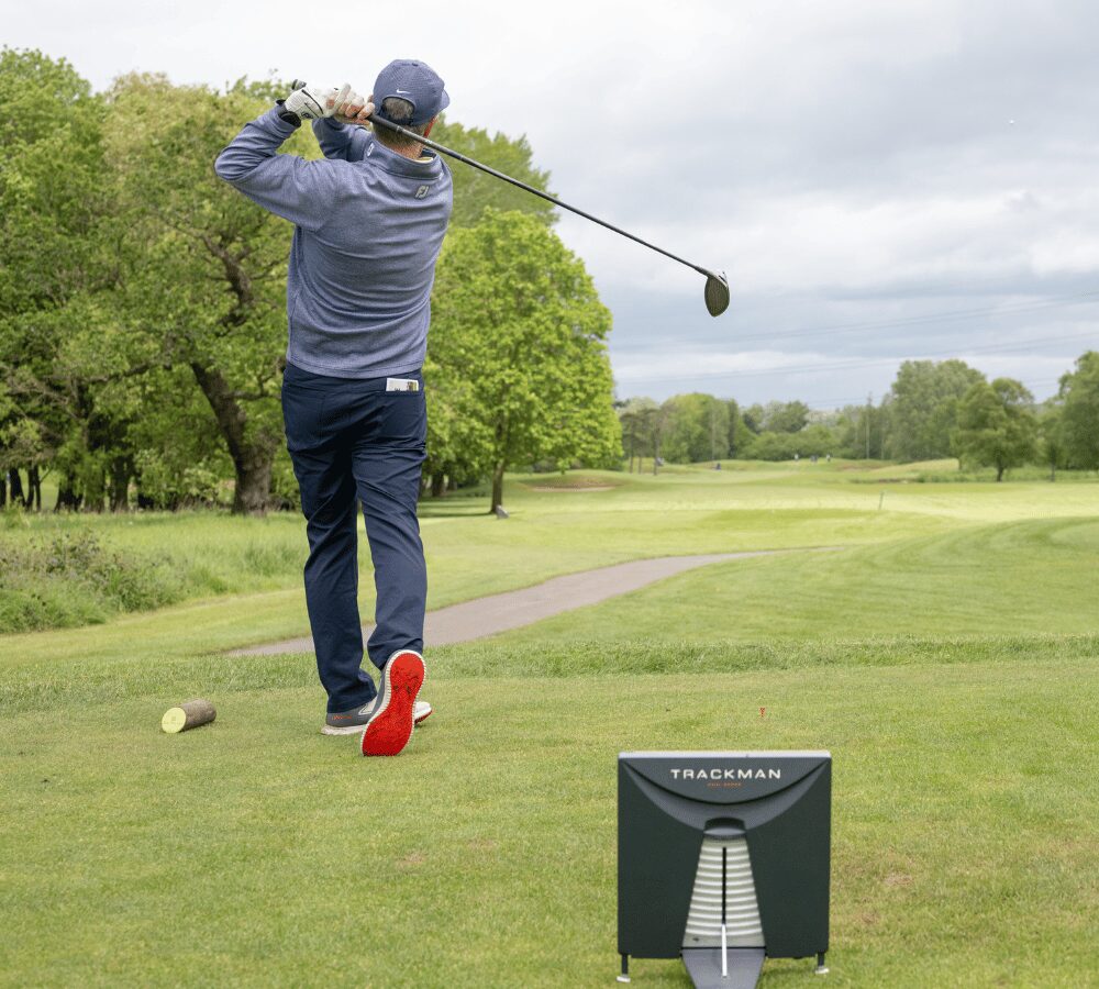 Golfer teeing off during a corporate golf day on a landscaped golf course.